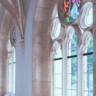 Old arched Catholic church corridor with white walls and with stained glass window in daylight