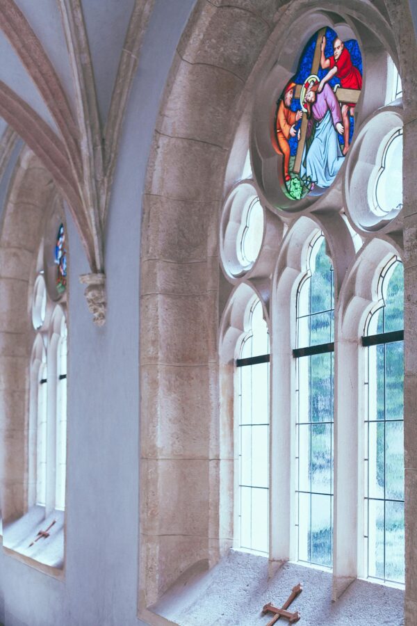 Old arched Catholic church corridor with white walls and with stained glass window in daylight